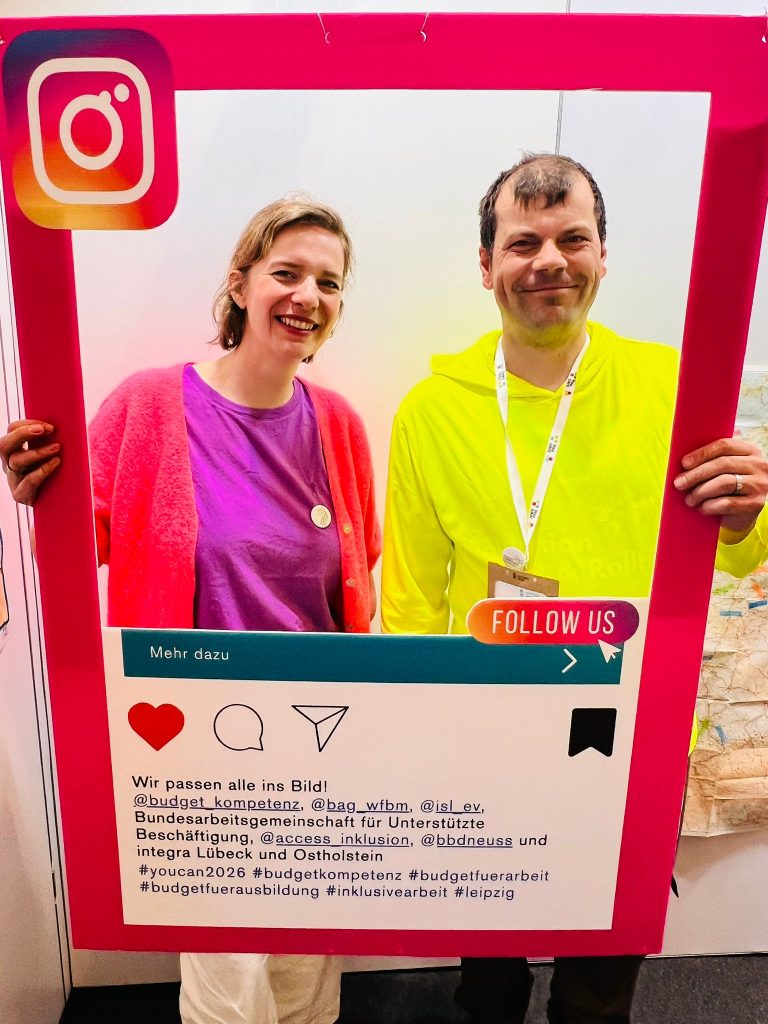 Wieder zwei Personen, die einen pinken Fotorahmen hoch halten. Sie lachen in die Kamera.