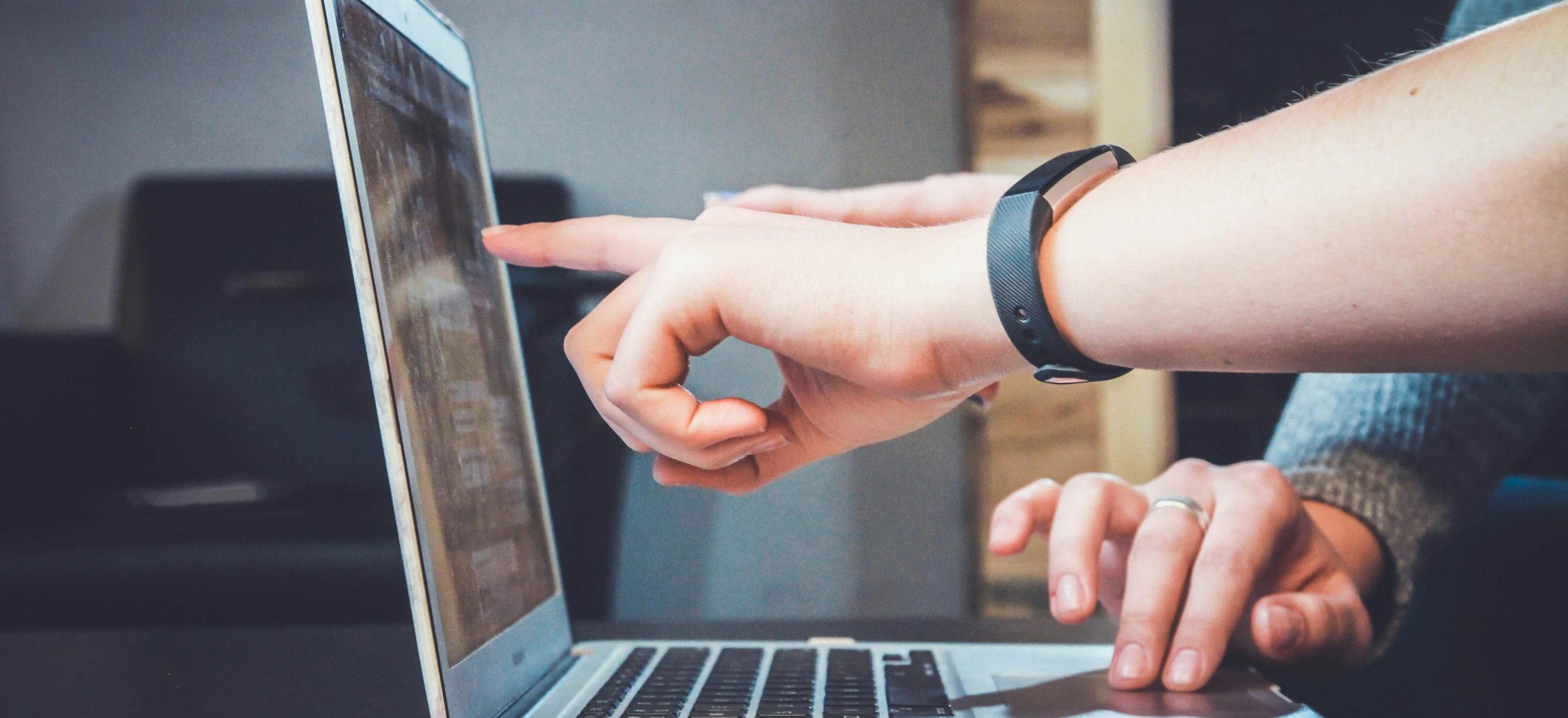 Eine Gesprächssituation. Abgebildet sind nur die Arme und Hände zweier Personen. Vor den Personen steht ein Laptop. Eine Hand deutet auf den Bildschirm, eine weitere fährt über die Tastatur.